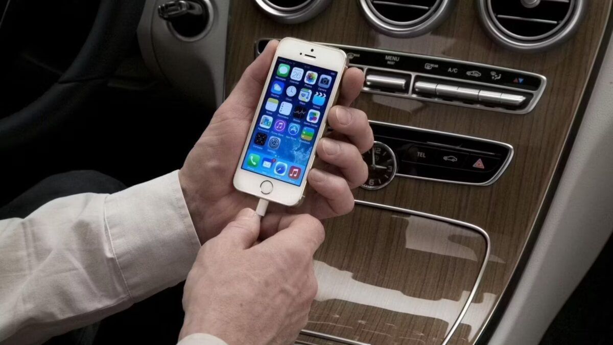 Человек держит iPhone подключённый к зарядке в машине