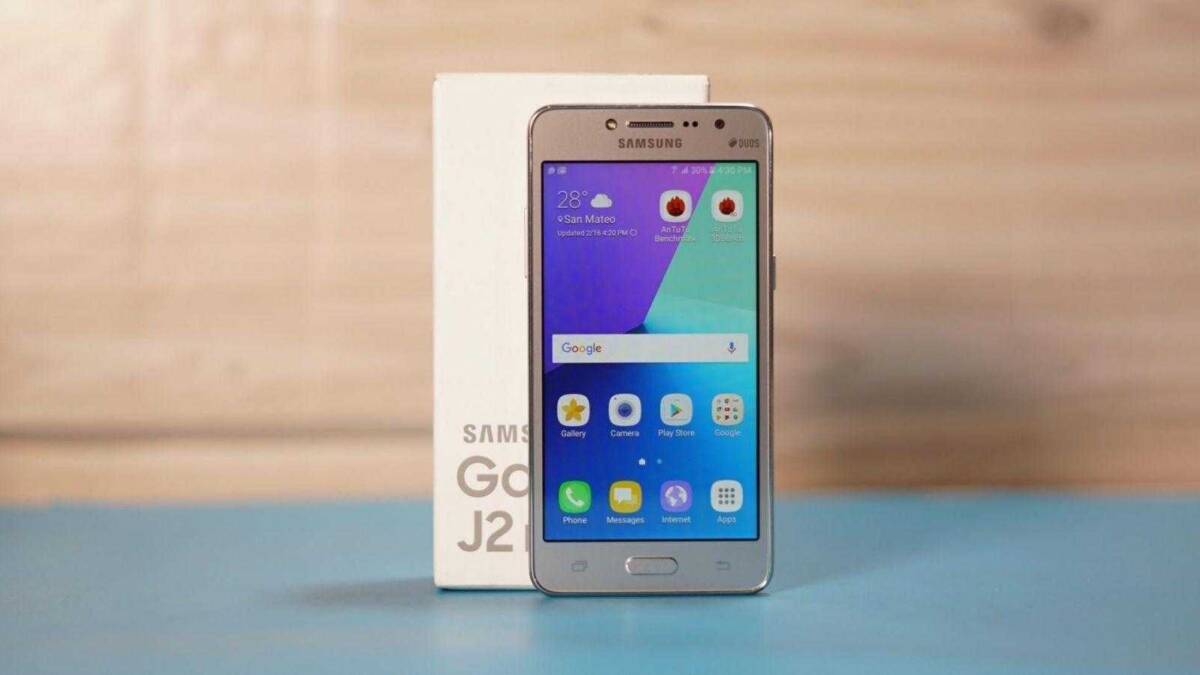 Смартфон Samsung Galaxy J2 на переднем плане перед белой коробкой