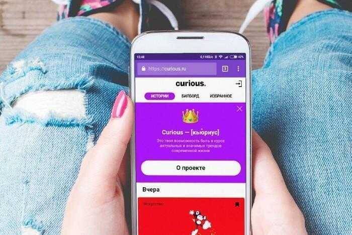 Смартфон с сайтом Curious на экране и джинсами