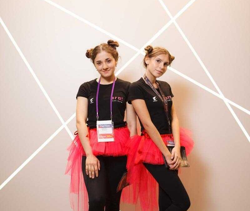 Две девушки в ярких юбках Тюльпан на фоне стены с логотипом iPhone