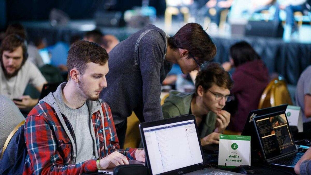 Люди за ноутбуками на хакатоне с логотипом ВКонтакте