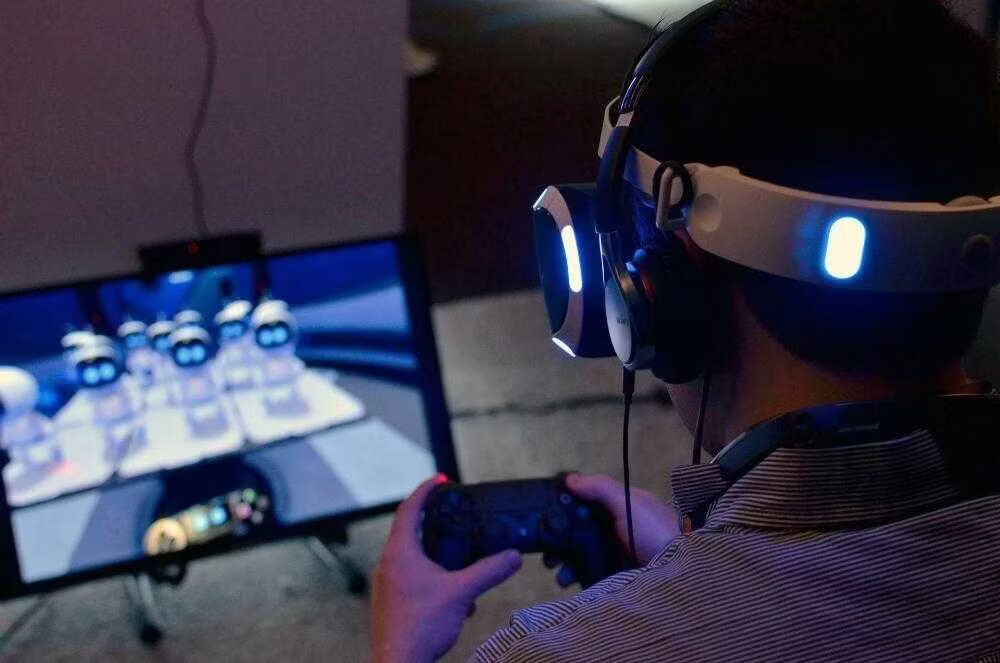 Пользователь с игровым шлемом PS VR и контроллером смотрит игровые сцены на мониторе
