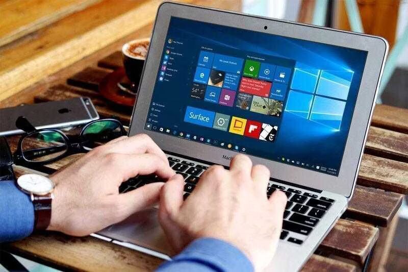 Человек использует MacBook на деревянном столе с запущенным Windows 10