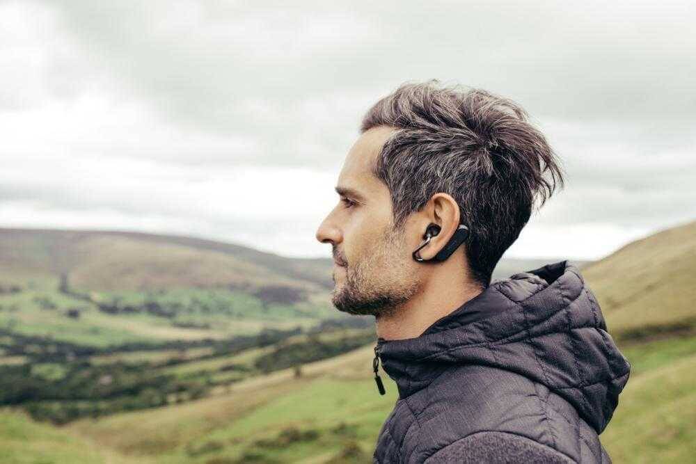 Мужчина в спортивной куртке с наушниками Xperia Ear Duo на фоне природы