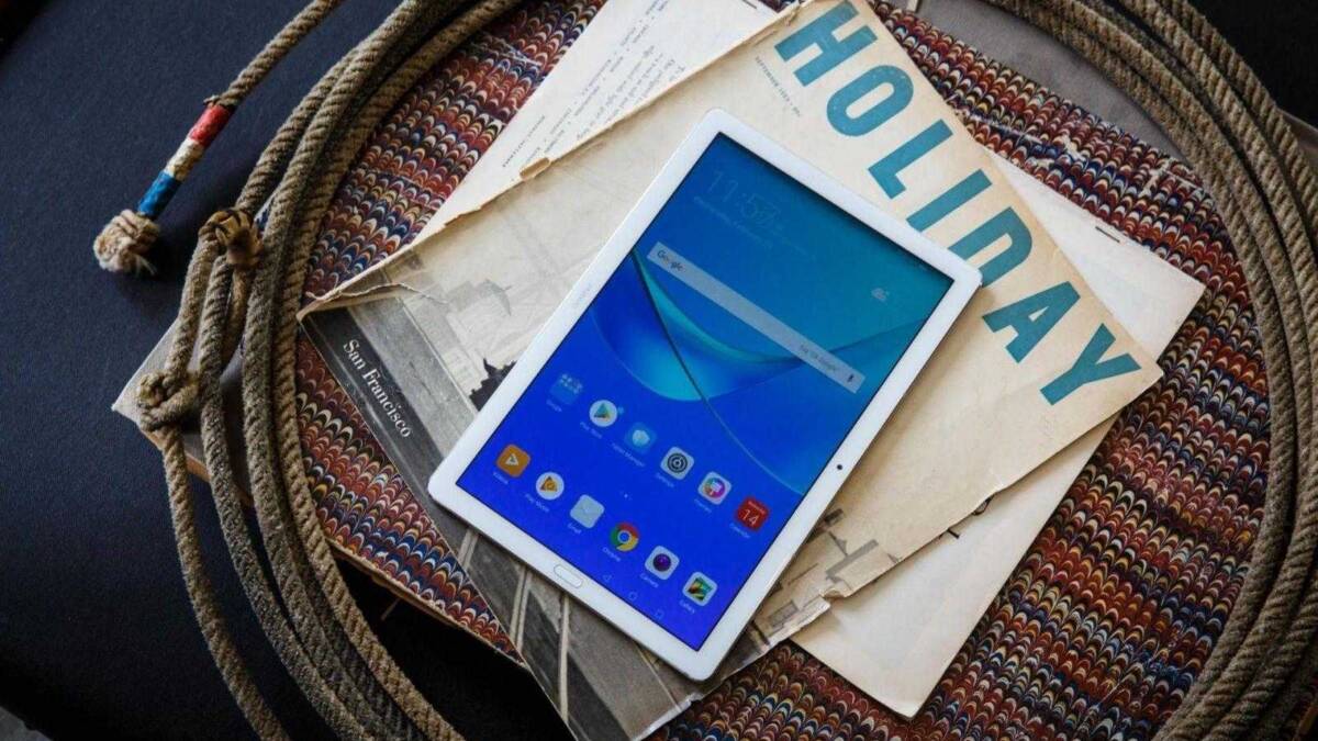 Планшет Huawei MediaPad M5 лежит на книге и газете