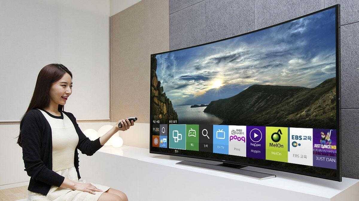 Женщина управляет 스마트 TV с помощью пульта дистанционного управления