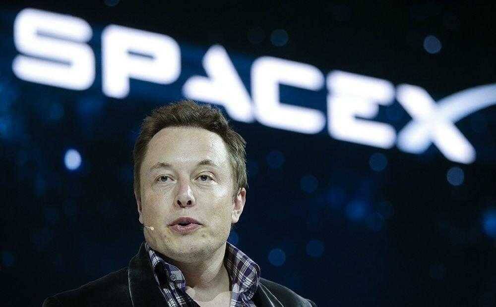Изображение Илона Маска на мероприятии в темном фоне с логотипом SpaceX