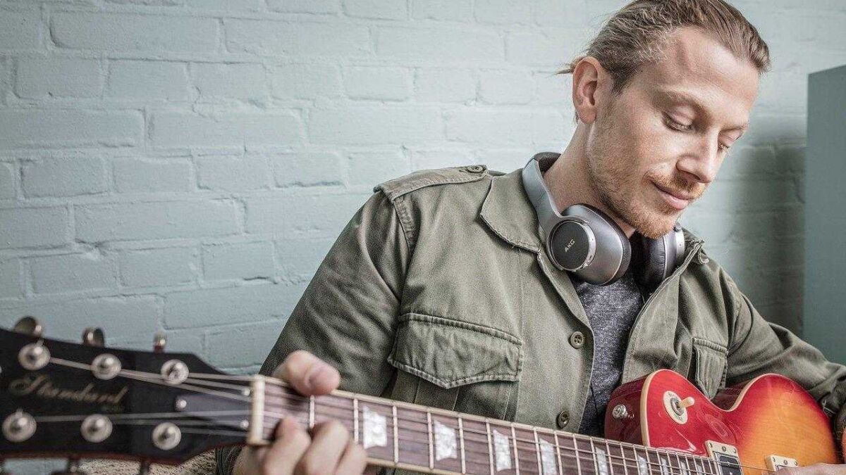 Мужчина с наушниками AKG и гитарой в руке