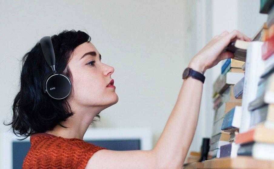 Девушка с чёрными короткими волосами и наушниками AKG на голове ищет книгу на полке