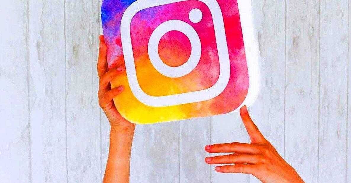 Люди держат ручки и держат в руках знак Instagram из красочного картона