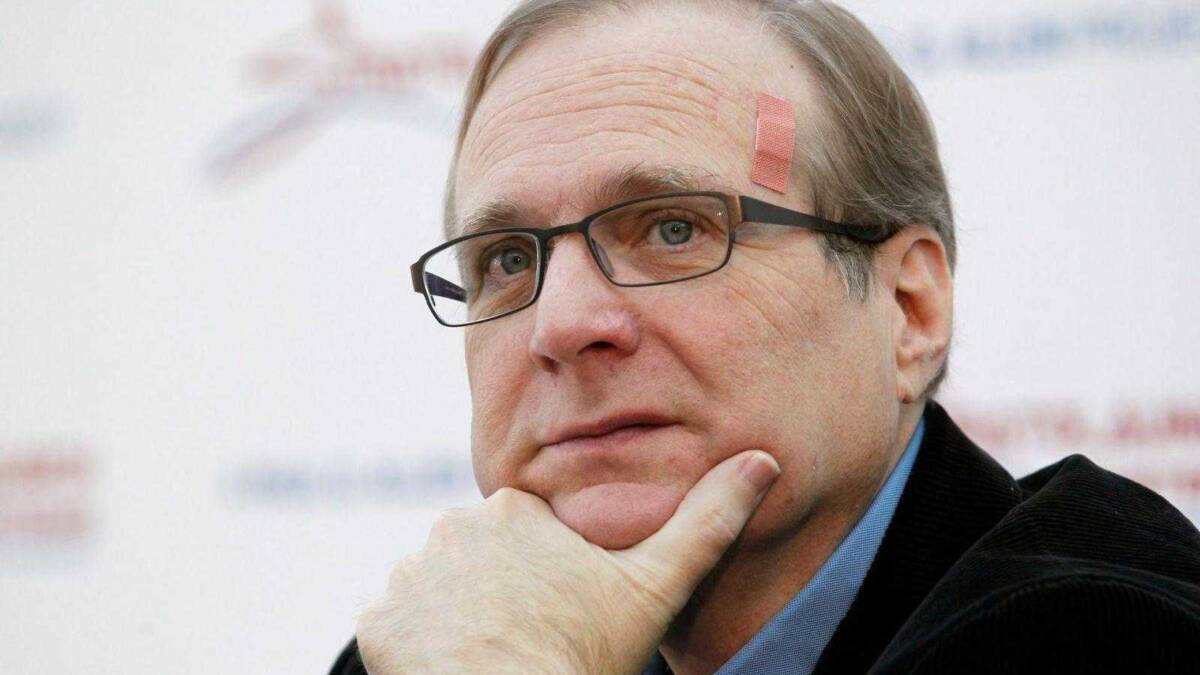 Умер cоучредитель Microsoft Пол Аллен 3 Мужчина в очках с бровью и рукой на лице смотрит в сторону на фоне рекламного баннера