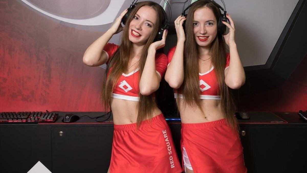 Две девушки в красных спортивных костюмах с наушниками за компьютером в игровой зоне
