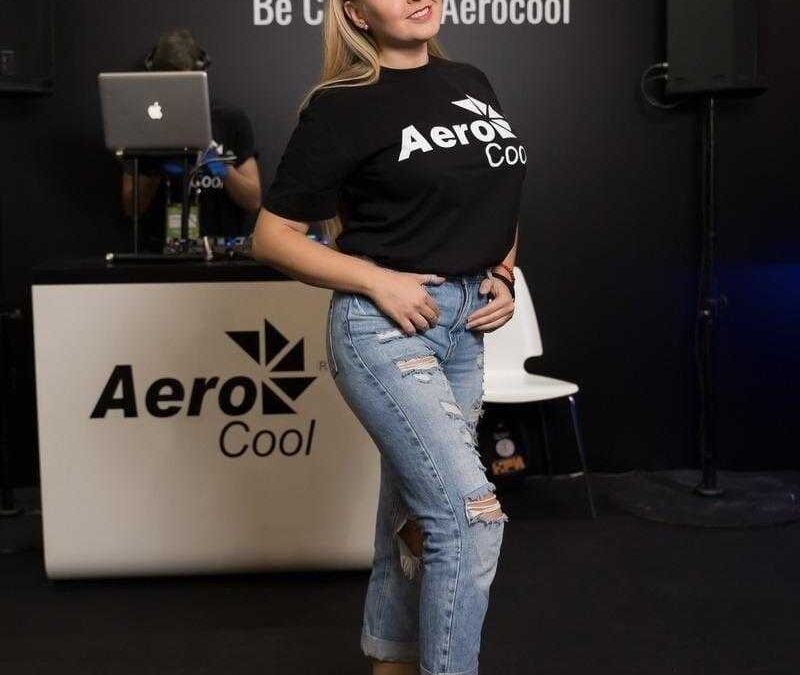 Девушка с рогами в чертой футболке AeroCool и рваными джинсами на выставке