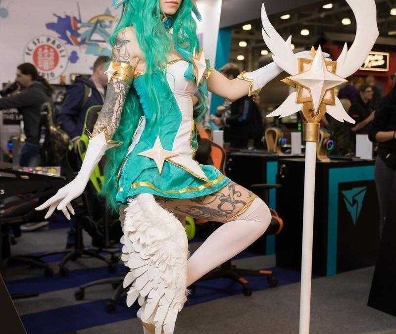 Косплей персонажа с зелеными длинными волосами и рогом возле выставочного стенда на ИгроМир 2018