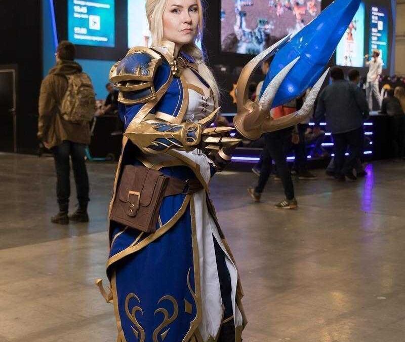 Косплей персонажа из игры с голубым мечом и золотыми доспехами на игровой выставке