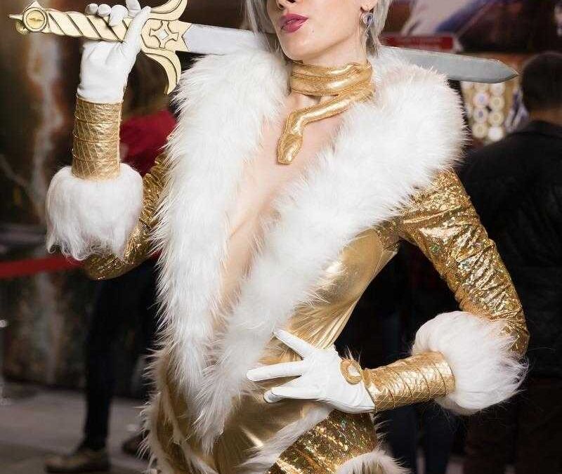 Женщина в золотом костюме с белой меховой отделкой держит меч на выставке ИгроМир 2018