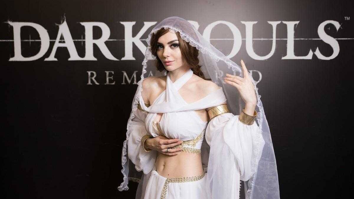 Девушка в белом костюме с золотыми украшениями у фона Dark Souls ремастер