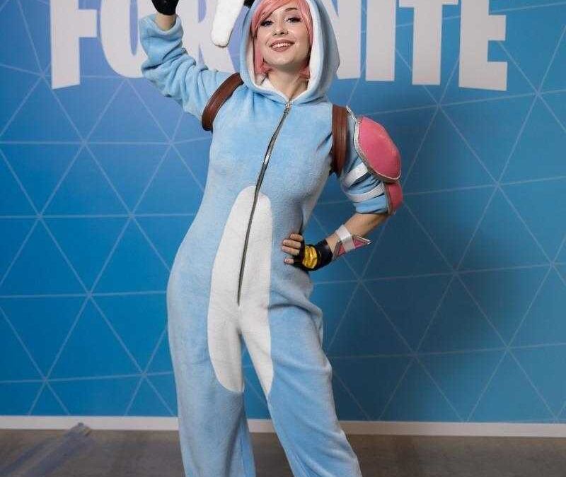 Косплей в костюме синего пижамного кролика с ушами на фоне стены с логотипом Fortnite