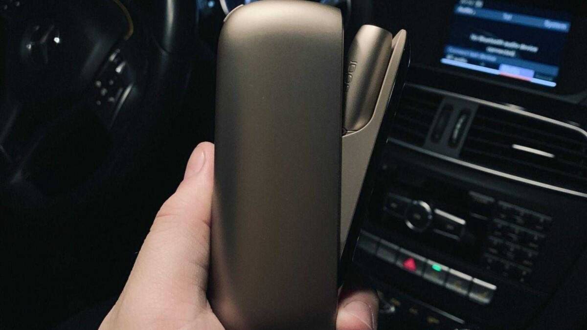 Рука держит устройство IQOS 3 в автомобиле