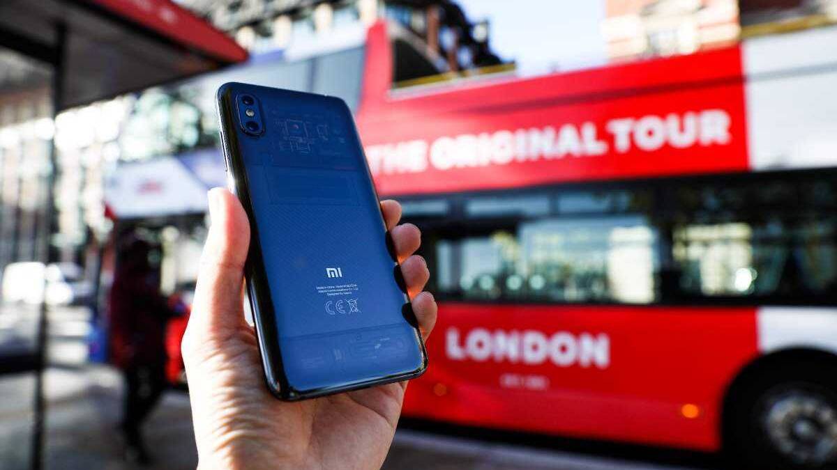 Рука держит смартфон Xiaomi Mi 8 Pro на улице на фоне красного автобуса с надписью London