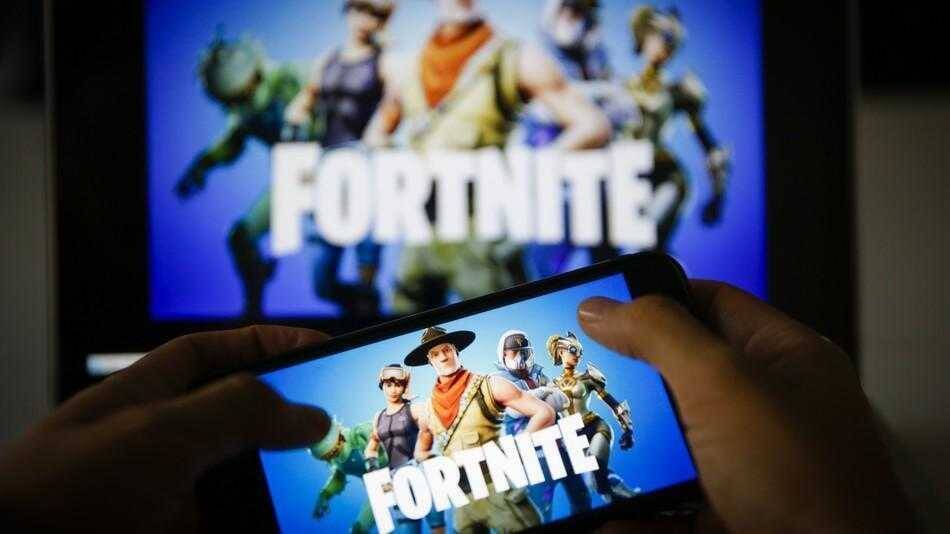 Человек держит смартфон с изображением Fortnite на экране