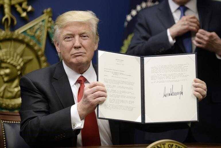 Дональд Трамп показывает подписанный документ в кабинете