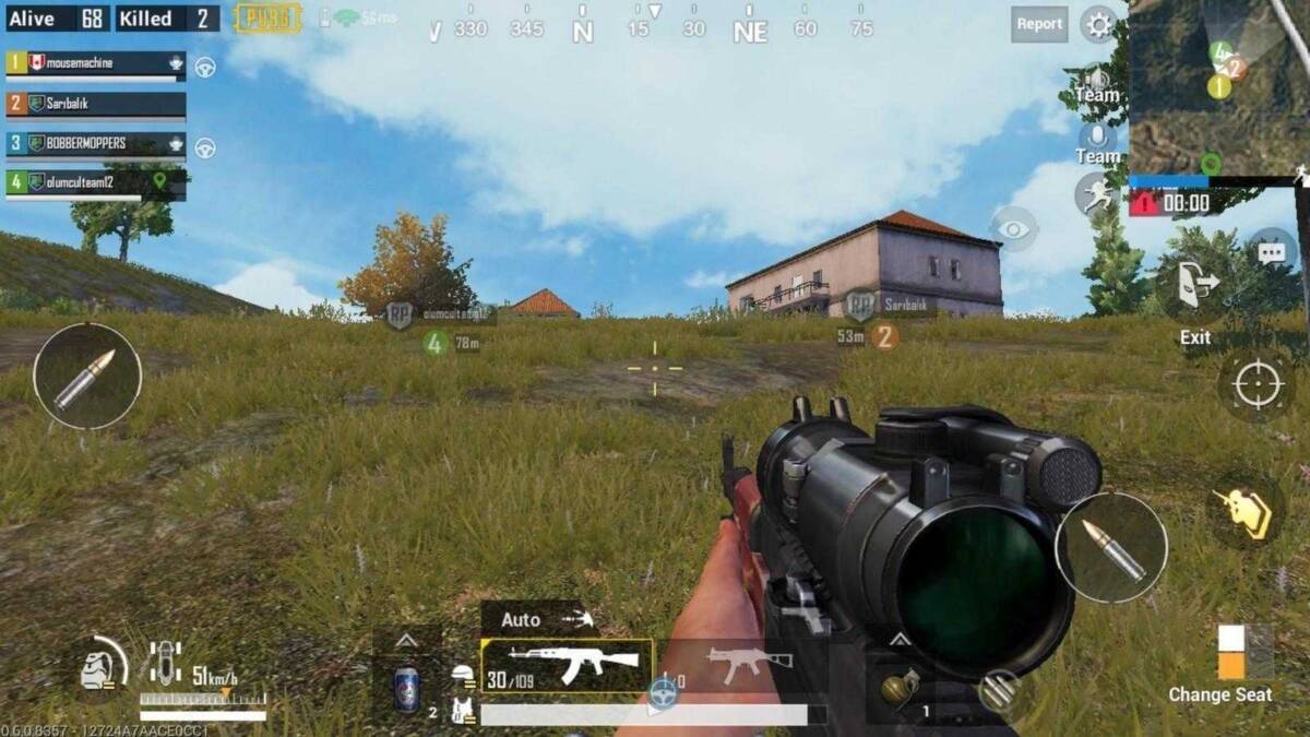 Экран мобильного телефона с игрой PUBG на фоне зеленой травы и домов