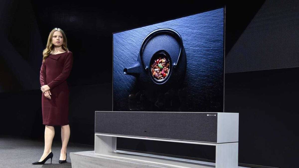 Женщина в бордовом платье стоит у телевизора LG Rollable OLED на сцене