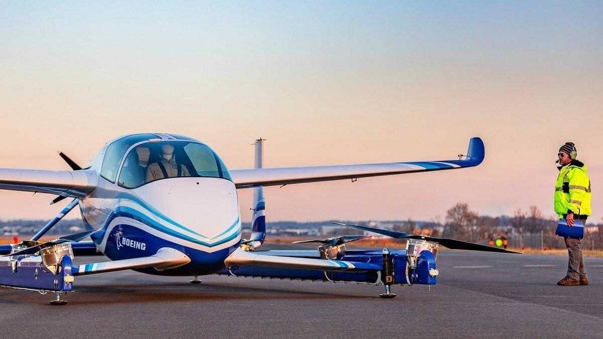 Беспилотное такси Boeing на взлётной полосе с человеком в жилете и наушниках