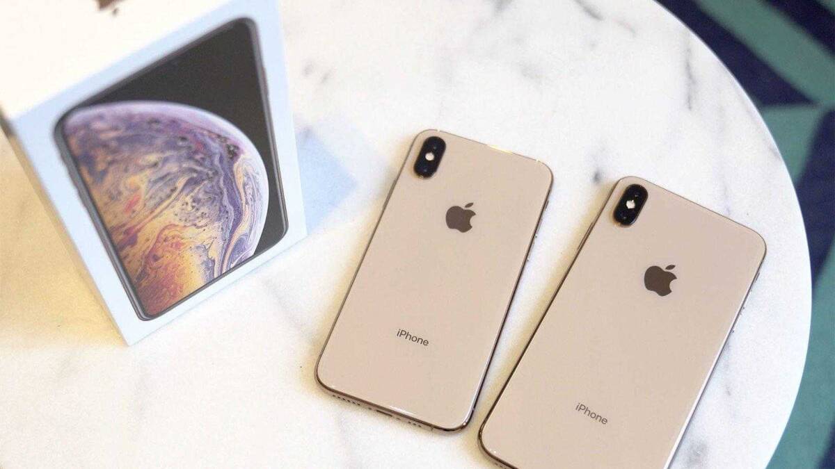 Два белых iPhone на белом круглом столе рядом с коробкой iPhone