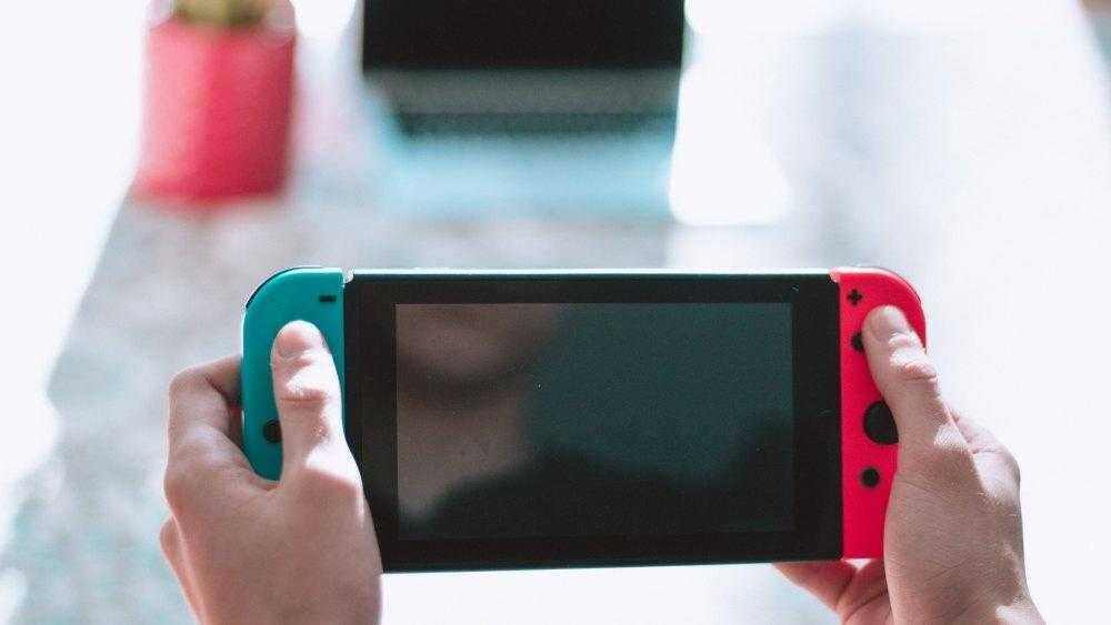 Человек держит игровую консоль Nintendo Switch с ярко-синей и красной боковыми панелями