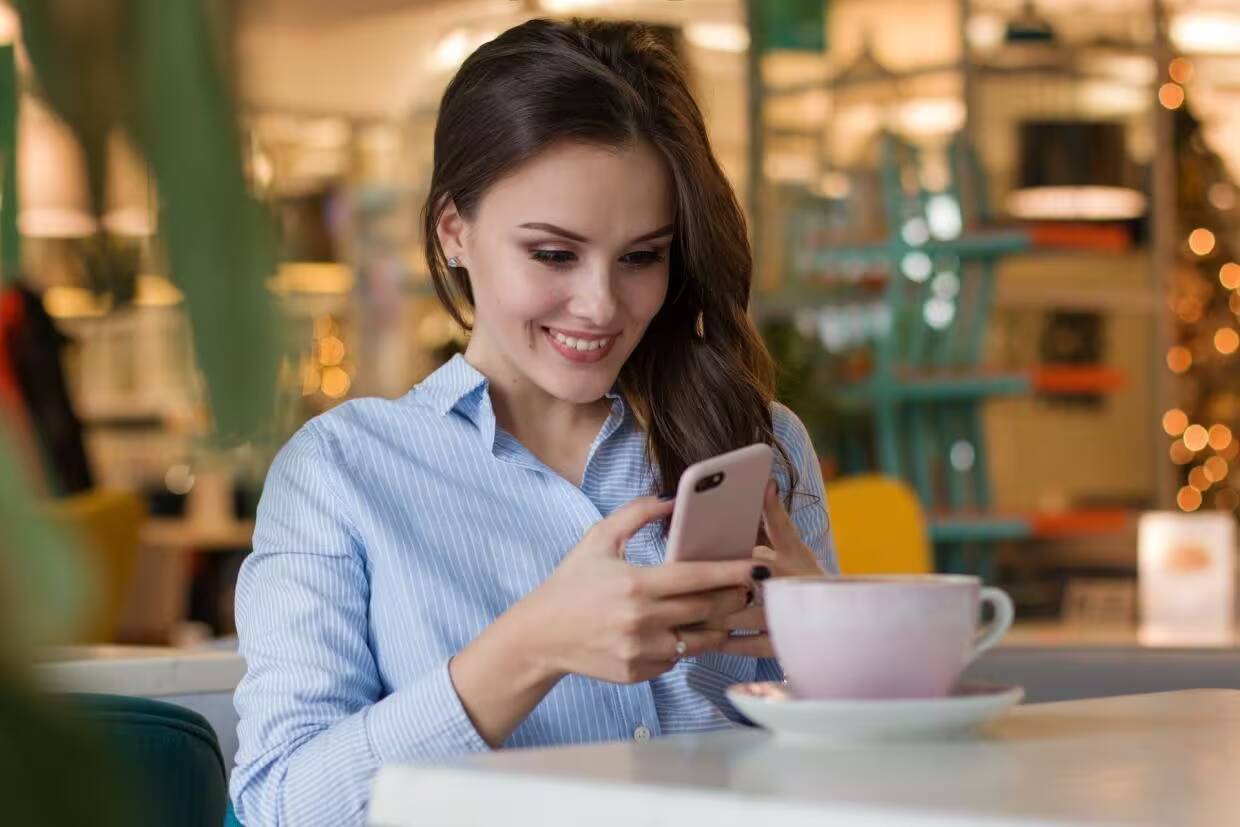 Девушка улыбается и использует смартфон в кафе