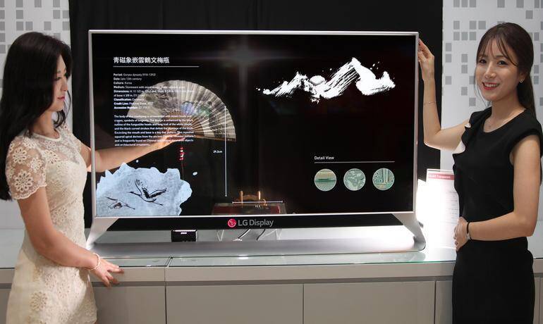 LG Display выпустит прозрачный OLED-экран 5 Две женщины показывают большой телевизор LG Display с изображениями природы и научной информации