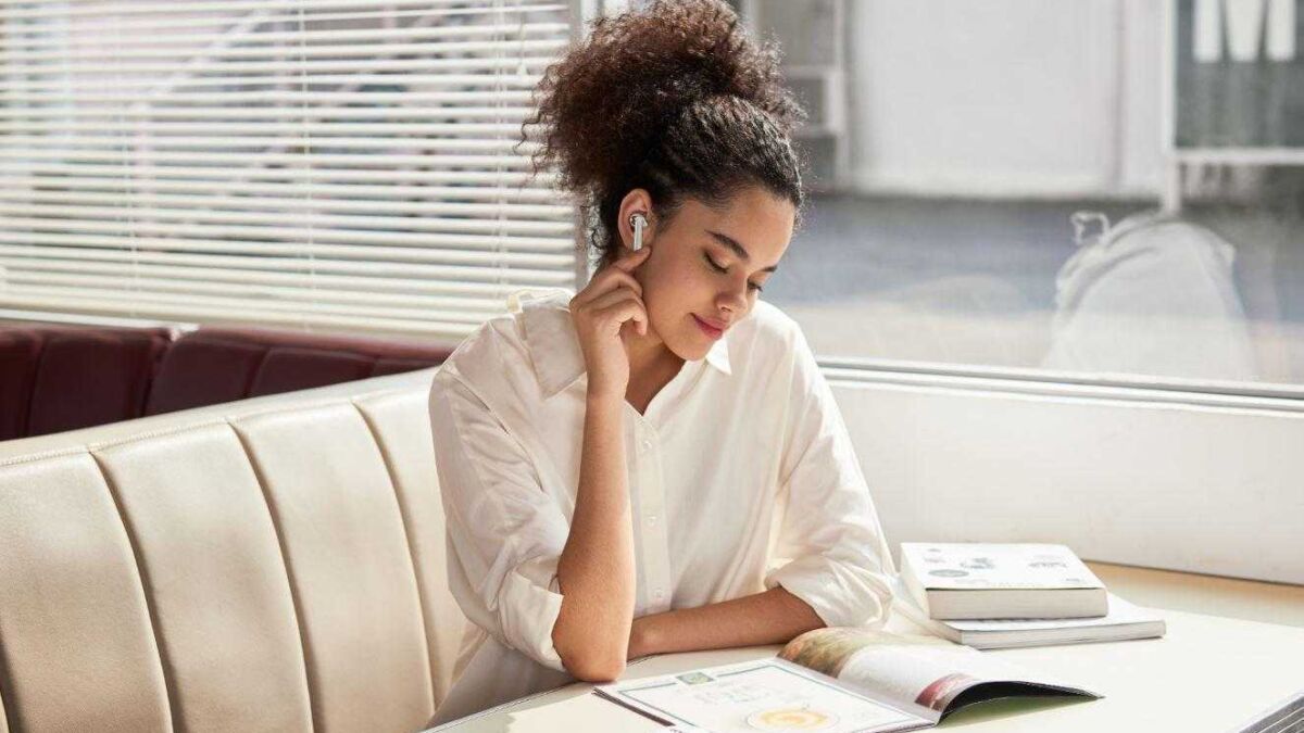 Девушка с наушниками читает журнал у окна на кухне