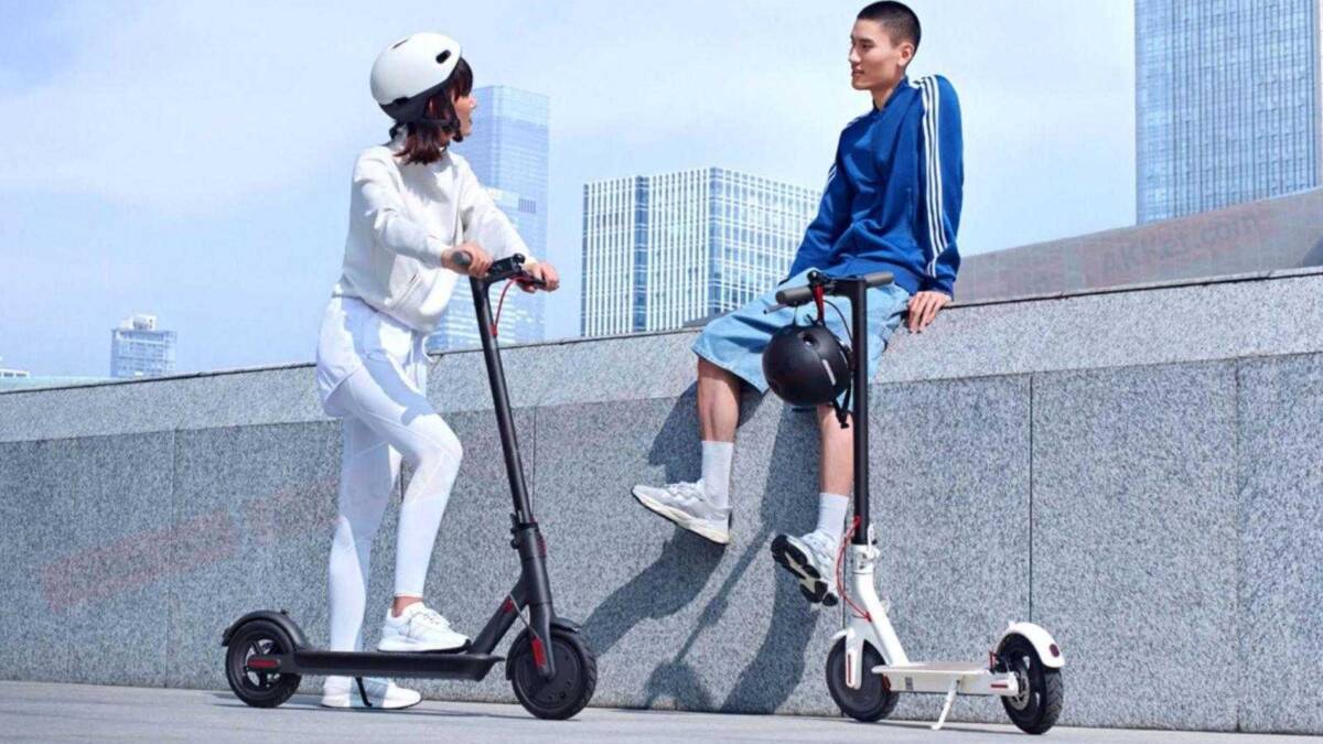 Xiaomi выпускает электросамокат Mijia Scooter 1S за 282 доллара 4 Девушка на электросамокате Xiaomi 10 Mi Youth Edition и парень с электросамокатом на фоне городских зданий