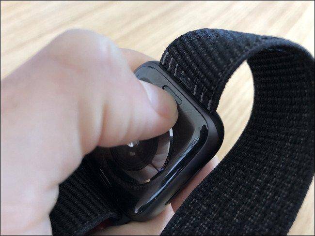 Как очистить и дезинфицировать часы Apple Watch 7 Рука держит Apple Watch с черным ремешком и кнопкой сбоку