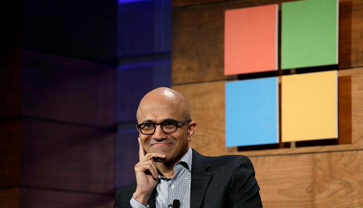 Человек в очках и деловом костюме на фоне логотипов Microsoft