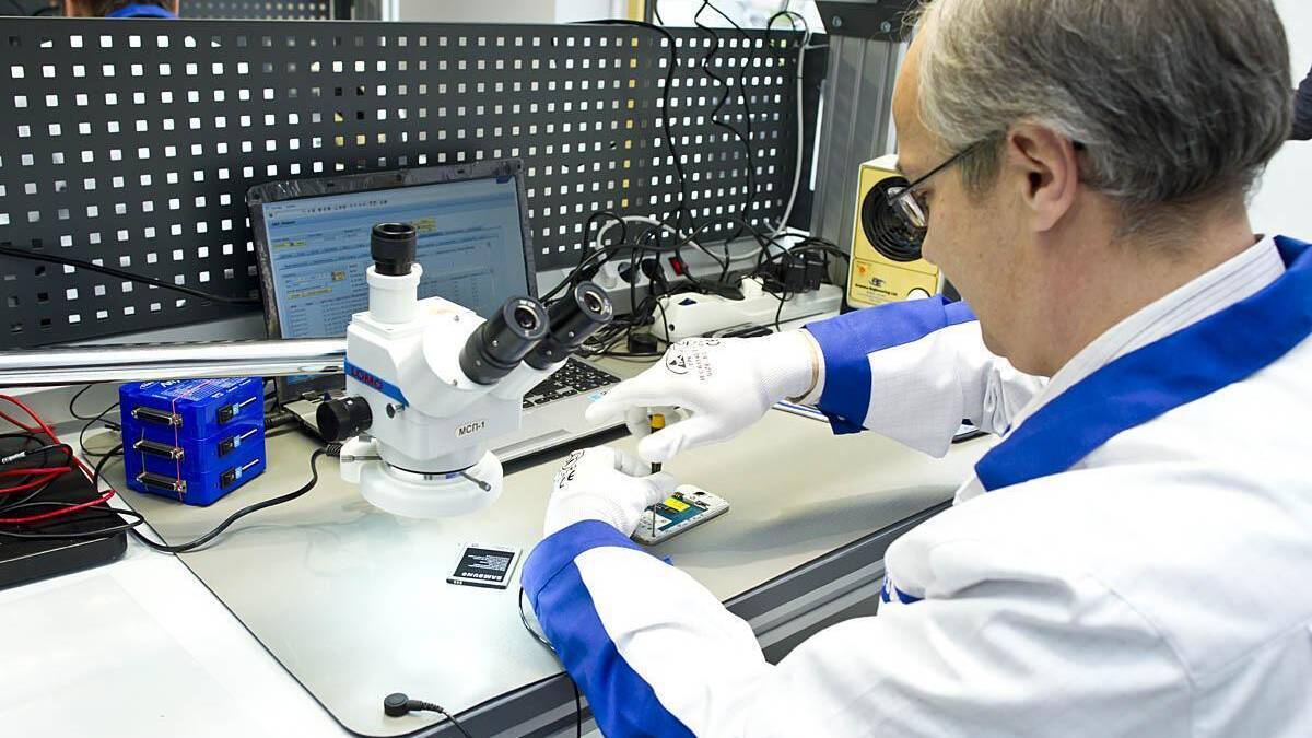 Механик работает с микроскопом и мобильным устройством в лаборатории