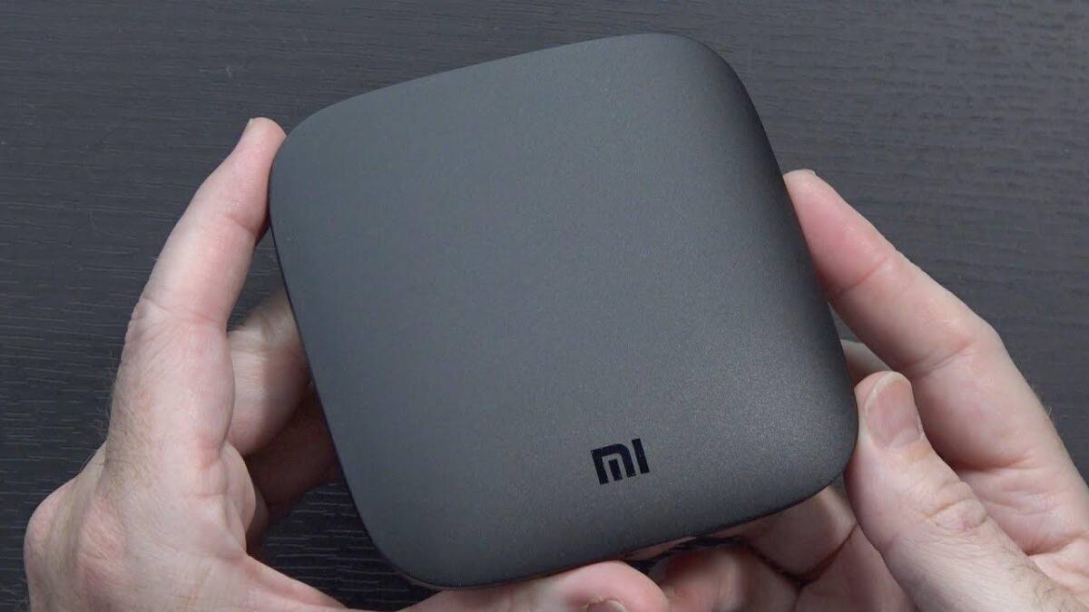Черная квадратная ТВ-приставка Xiaomi Mi Box в руке