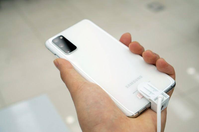 Белый смартфон Samsung Galaxy S20 Ultra на руке с зарядным устройством