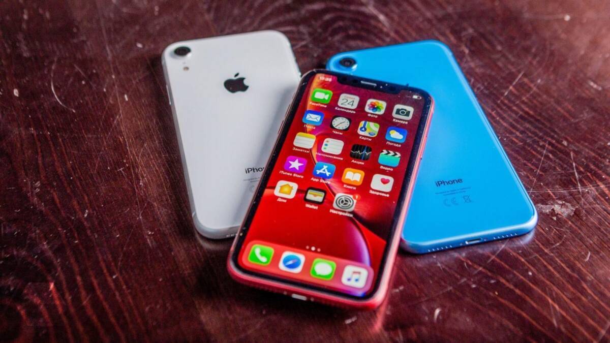 Три iPhone на деревянной поверхности, один с активным экраном