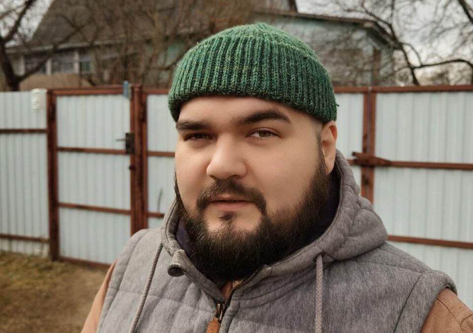 Мужчина в серой жилетке и зеленой шапке с телефоном