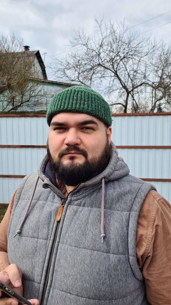 Человек в зелёной шапке и жилете на улице