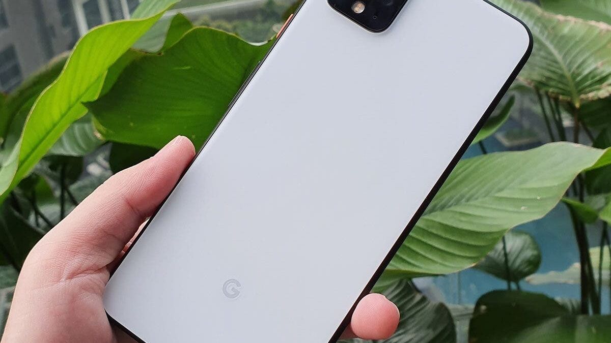 Белый смартфон Google Pixel 4 в руке на фоне зелёных листьев