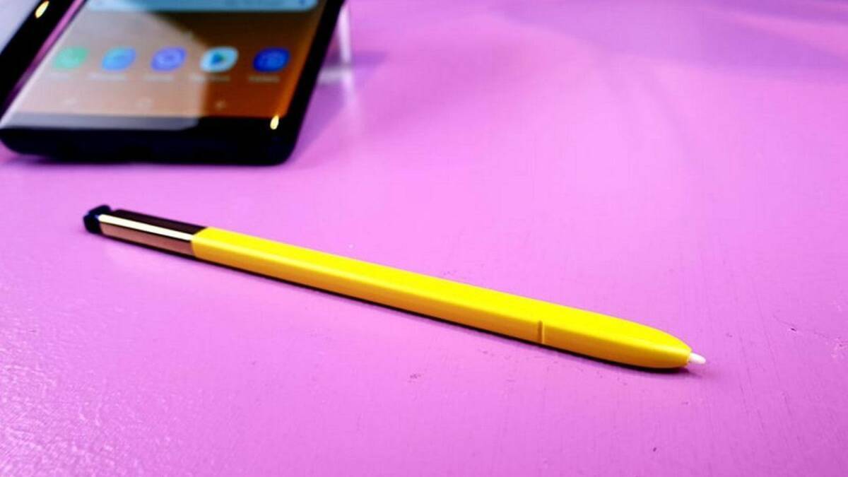 Жёлтый стилус S Pen на розовом столе и смартфон в уголке