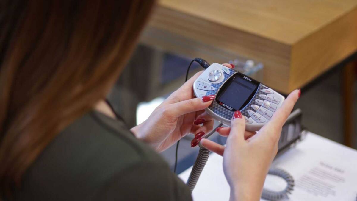 Рука держит старый мобильный телефон Nokia с кабелем на фоне стола