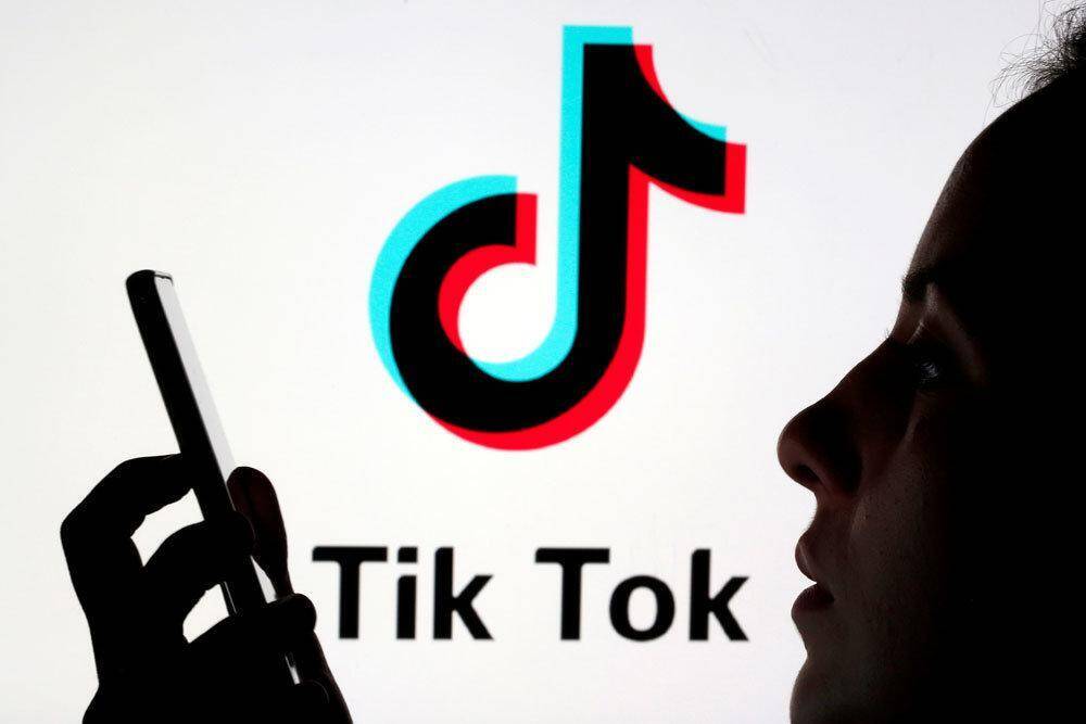 Силуэт человека с телефоном у экрана с логотипом Tik Tok