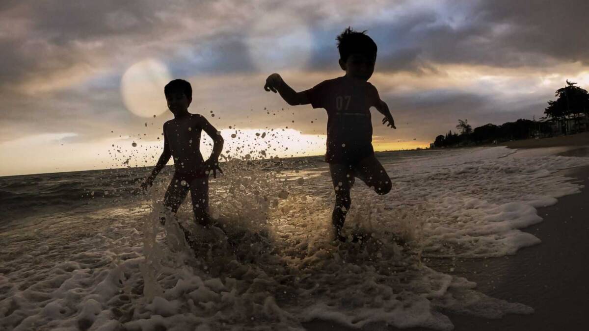 Два ребёнка играют в воде на пляже во время заката с тёмным облачным небом