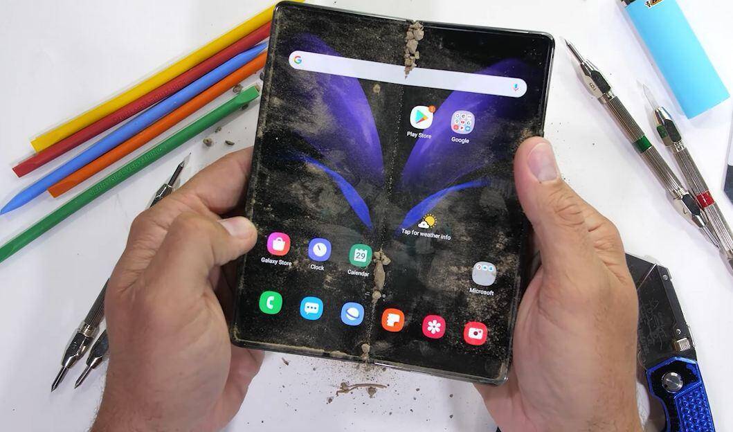 Изображение сгибающегося смартфона Galaxy Z Fold 2 с грязью на экране и руке держит устройство