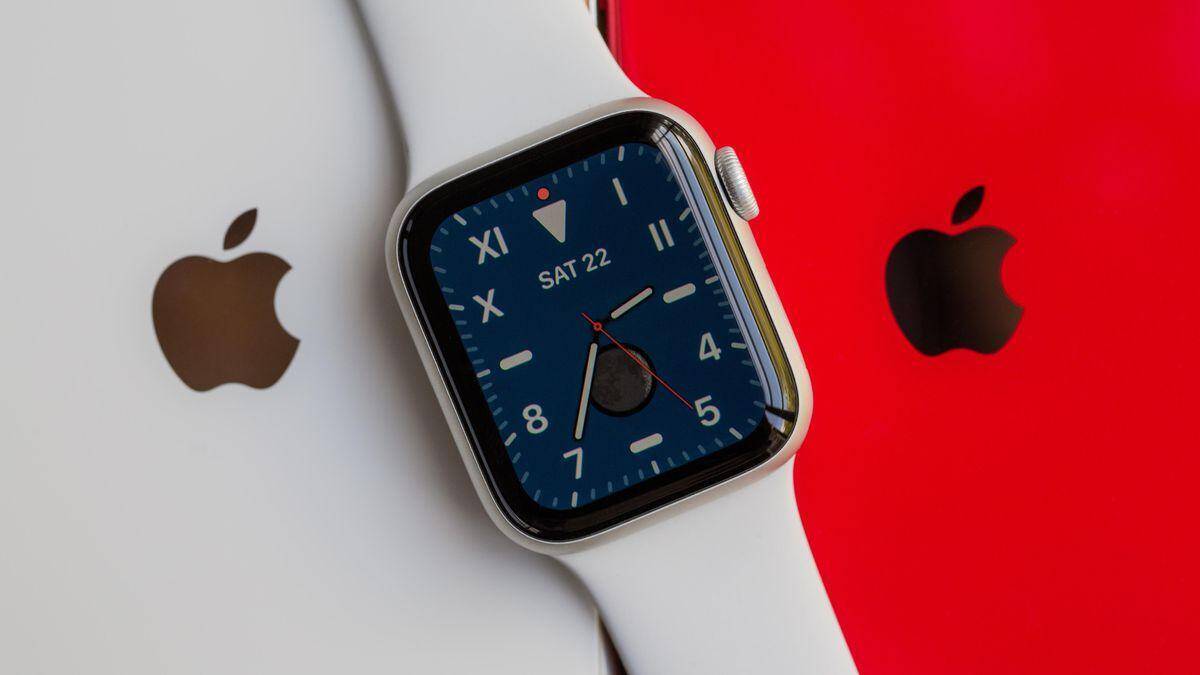 Умные часы Apple Watch SE с белым ремешком и черным дисплеем на фоне белого и красного устройств